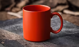 an orange mug with some sort of design on top of a piece of wood