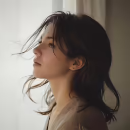 a woman with long brown hair is standing near the window