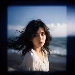 a woman standing near the ocean with her hair flying in the wind