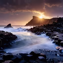 a sunset is seen through the clouds over rocks and ocean