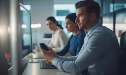 a man with a cell phone next to a woman at a desk