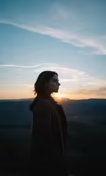 a person standing on a hill with the sun in the distance
