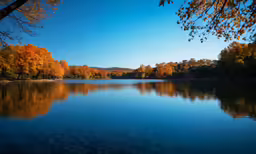 a large lake surrounded by colorful trees with a blue sky