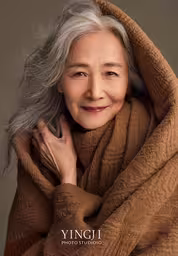 the old woman is posing in front of the camera,an old woman with grey hair and a brown blanket