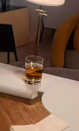 a glass with liquor sits next to a plate with napkins