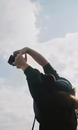 a woman holding up a camera in front of clouds