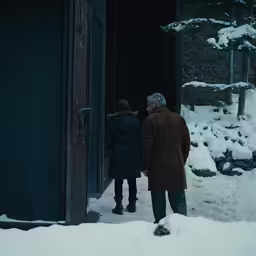 two people stand next to an open door and look into the snow