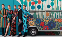 five women in bright outfits next to the side of a colorful bus