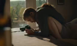a woman kneeling on the floor holding a camera looking through a window