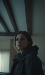a woman in a green jacket standing in a dark room