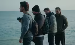 a group of men stand on a beach and talk