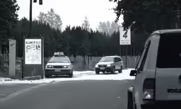 two cars driving through a snowy street next to a forest