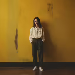 a woman is standing against a wall in front of a yellow wall