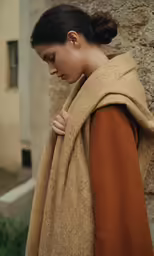 a woman wearing an orange coat standing by a building