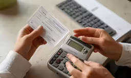 a person sitting at a table with a calculator and a receipt