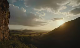 the sun is setting in the distance near a large cliff