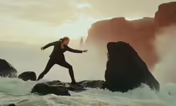 a woman wearing black is running on a rock in front of the ocean