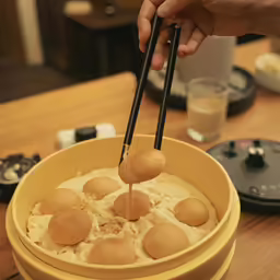two hands holding chopsticks over a yellow bowl filled with food
