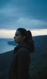 woman standing on hillside overlooking ocean in stormy weather