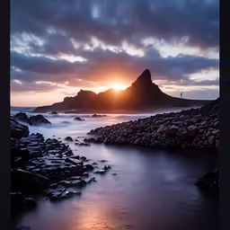 a view of some rocks at a beach with the sun going down