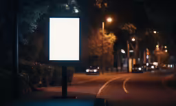 a lit street sign is standing next to the road