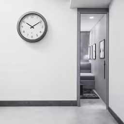 a white hallway with a black clock next to a white wall
