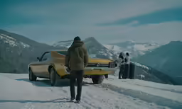 a person is standing in the snow with a yellow car and some people looking at them