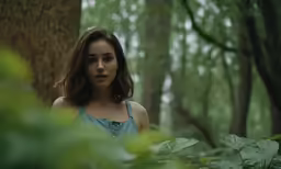 a young woman standing in the woods looking off into the distance