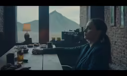 a woman at a table looking out a window with mountains in the background