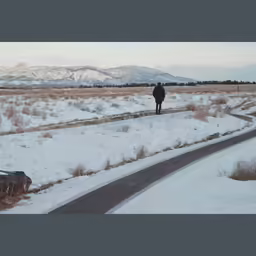 a man walking across a snow covered field next to trees