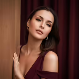 the woman wearing a dress looks out from behind a curtain