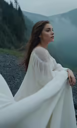 a woman in a long, flowing white gown poses with her arm over her shoulder