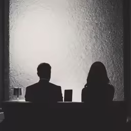 two people sit on the opposite side of a table and look at a lamp that has been illuminated by a bulb
