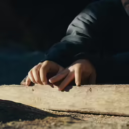 the hands of a person sitting on the side of a tree trunk