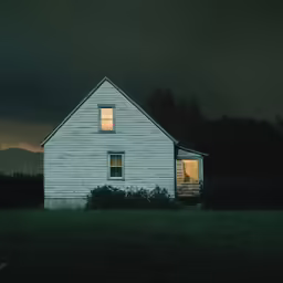 an old white house sits at night on the grass and bushes