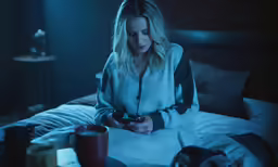 a woman sits on a bed looking at her cell phone