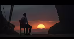 there is a man sitting on a chair looking at the sunset