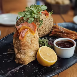a meal of bread, bacon and vegetables sitting on a plate with a side of sauce