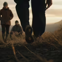 three people are walking in grass with boots on