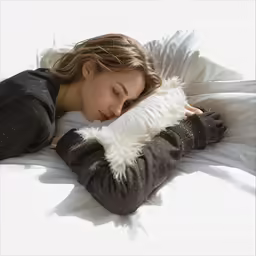 woman in black sweater laying down holding a furry white pillow