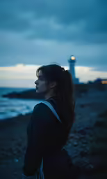 a woman standing on a beach at sunset with a lighthouse in the background