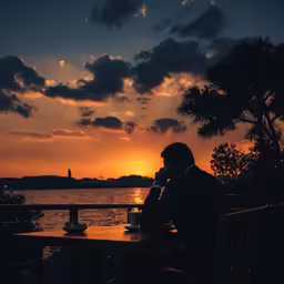 a person sits on a bench while the sun sets