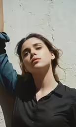 a woman leaning against a white wall and wearing a black shirt