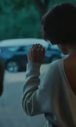 a girl sitting on a street corner, looking into a car