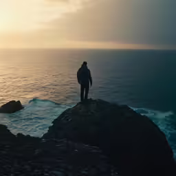 man standing on a rock near the ocean at sunset
