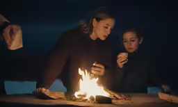 two women are sitting around a fire outside