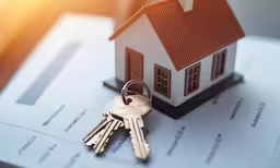 keys are placed on top of a house model that is resting on top of paperwork