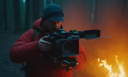 a person holding a video camera in front of a fire