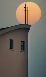 the sun is setting behind a building and a cross