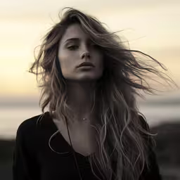 woman standing in front of an ocean with her hair blowing,a woman that is standing up with her hair blowing in the wind